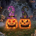 Two lighted jack-o'-lantern yard signs in purple witch hats
